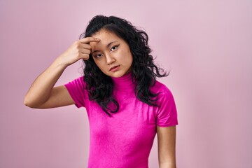 Young asian woman standing over pink background pointing unhappy to pimple on forehead, ugly infection of blackhead. acne and skin problem