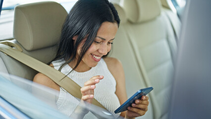 Young beautiful hispanic woman passenger using smartphone sitting on car at street