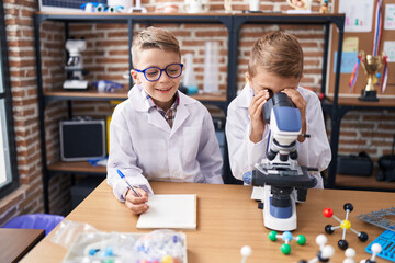 Adorable boys students using microscope writing notes at laboratory classroom