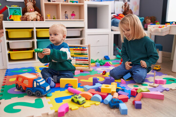 Adorable boy and girl playing with construction blocks sitting on floor at kindergarten