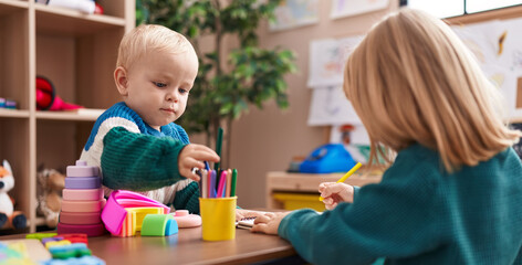 Adorable boy and girl preschool students sitting on table drawing on paper at kindergarten