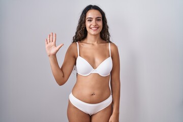 Fototapeta premium Young hispanic woman wearing white lingerie showing and pointing up with fingers number five while smiling confident and happy.