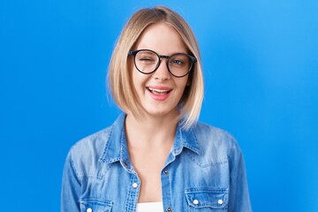 Young caucasian woman standing over blue background winking looking at the camera with sexy expression, cheerful and happy face.