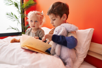 Adorable boy and girl reading book sitting on bed at bedroom