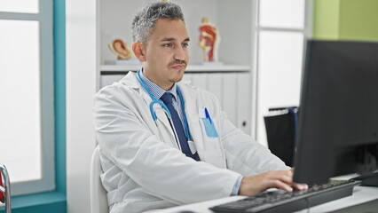 Naklejka na ściany i meble Young hispanic man doctor using computer working at clinic