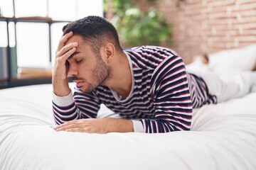 Young hispanic man stressed lying on bed at bedroom