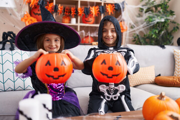 Fototapeta premium Adorable boy and girl having halloween party holding pumpkin basket at home