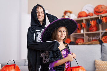 Adorable boy and girl having halloween party holding pumpkin basket at home