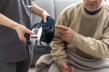 Smiling young nurse taking old man's blood pressure