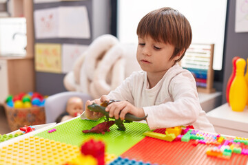 Adorable caucasian boy playing with dinosaur toy sitting on table at kindergarten