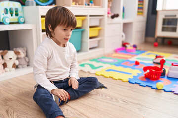 Adorable caucasian boy sitting on floor with relaxed expression at kindergarten
