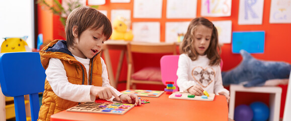 Adorable boy and girl playing with maths puzzle game sitting on table at kindergarten
