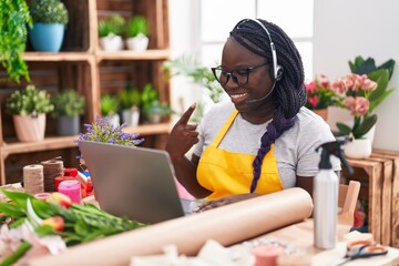 Young african woman working at florist shop doing video call smiling happy pointing with hand and finger
