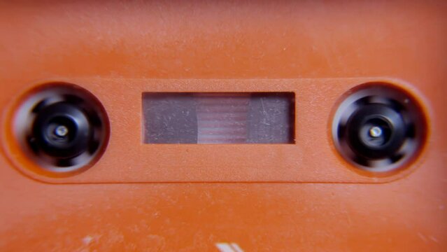 Rewinding an old orange plastic cassette tape inside a deck. Obsolete vintage audio technology. Front detail shot.
