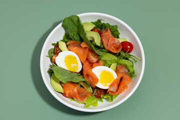 Fresh green salad with salmon and eggs on a green background