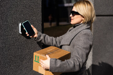 Smart home concept - close up of woman with box use mobile phone to open electronic lock