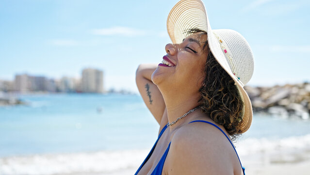 Young beautiful latin woman tourist smiling confident wearing swimsuit and summer hat at beach