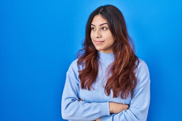 Obraz premium Hispanic young woman standing over blue background looking to the side with arms crossed convinced and confident