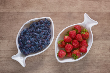 Strawberries and blueberries in porcelain cups on a wooden background. Berry mix. Dishes in the shape of the zodiac sign Pisces. Diet breakfast. Close up. Copy space.