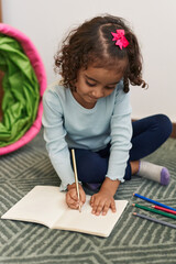 Adorable hispanic girl drawing on notebook sitting on floor at home