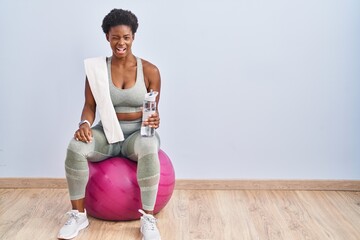 African american woman wearing sportswear sitting on pilates ball winking looking at the camera...