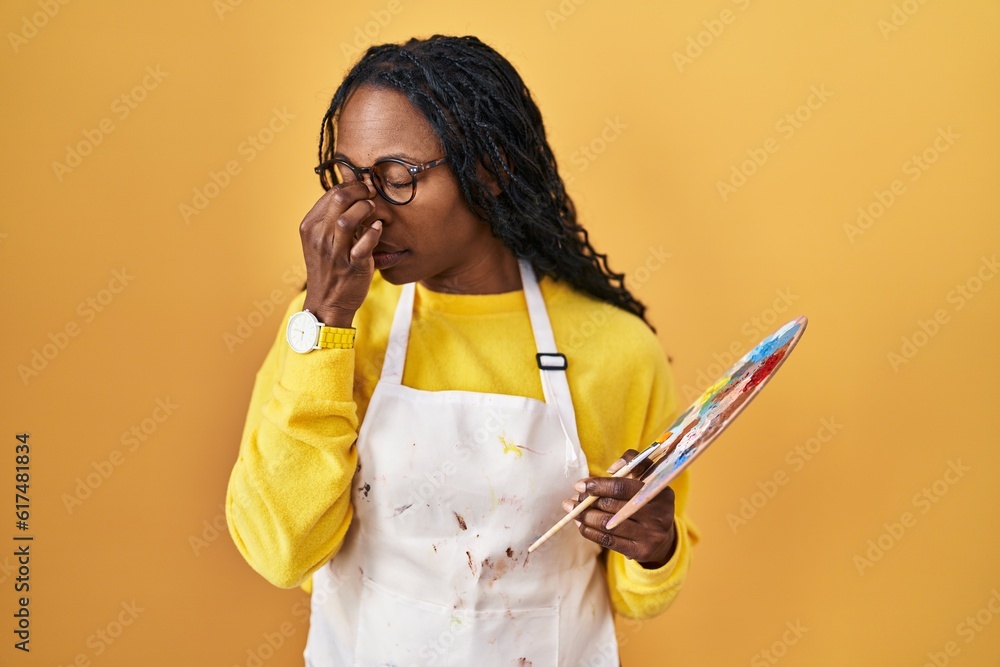 Wall mural African woman holding painter palette tired rubbing nose and eyes feeling fatigue and headache. stress and frustration concept.