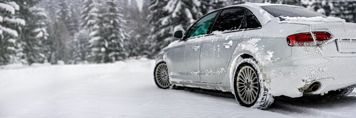 Silver car covered with ice parked on snow covered road, view from behind, blurred trees background...