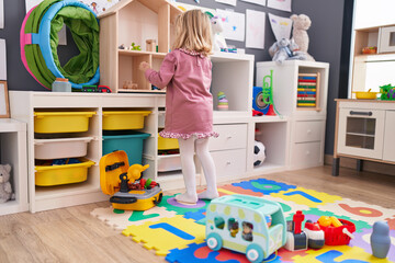 Adorable blonde girl playing with toys standing at kindergarten
