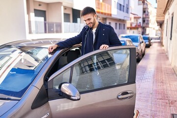 Young hispanic man smiling confident opening car door at street