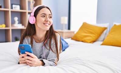 Young beautiful hispanic woman listening to music lying on bed at bedroom