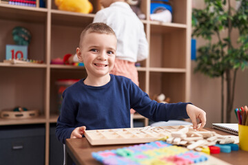 Adorable caucasian boy playing with puzzle game sitting on table at kindergarten