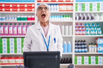 Middle age woman with tattoos working at pharmacy drugstore angry and mad screaming frustrated and furious, shouting with anger. rage and aggressive concept.