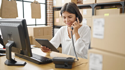 Young beautiful hispanic woman ecommerce business worker talking on telephone using touchpad at office