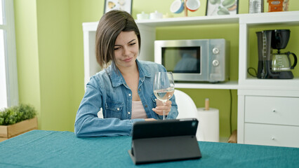 Young caucasian woman watching movie on touchpad drinking wine at home