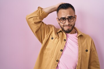 Young hispanic man standing over pink background confuse and wonder about question. uncertain with doubt, thinking with hand on head. pensive concept.