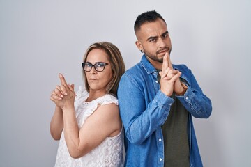 Hispanic mother and son standing together holding symbolic gun with hand gesture, playing killing shooting weapons, angry face