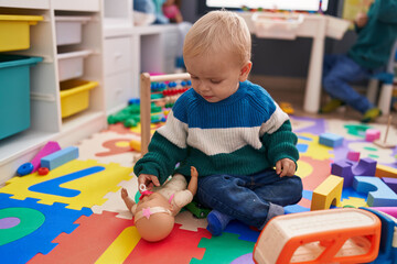 Adorable caucasian boy playing with toys sitting on floor at kindergarten