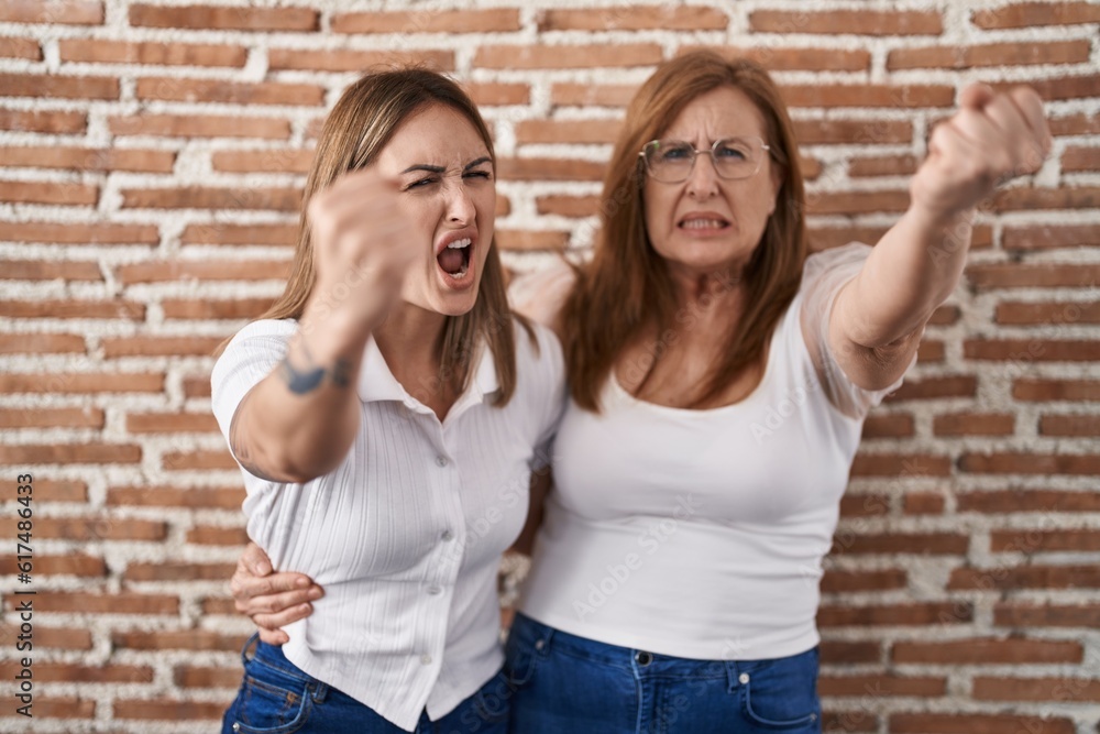 Poster hispanic mother and daughter wearing casual white t shirt angry and mad raising fist frustrated and 