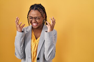 African american woman with braids standing over yellow background celebrating mad and crazy for...