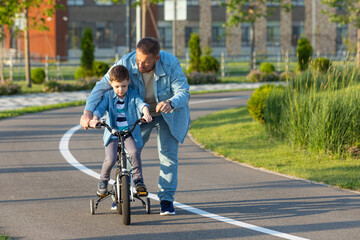 Father teaching son riding bike. Father helping excited son to ride a bicycle in american...