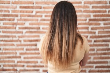 Young brunette woman standing over bricks wall standing backwards looking away with crossed arms