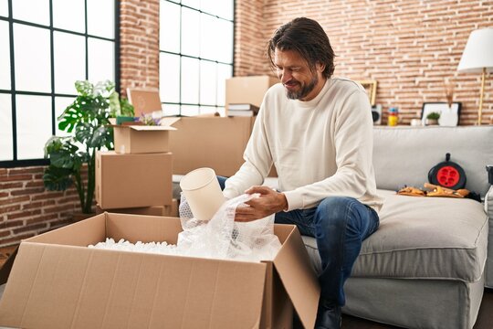 Middle age man smiling confident unpacking cardboard box at new home