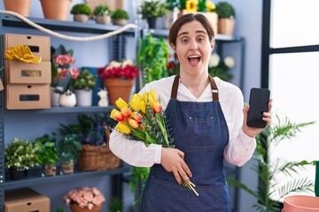 Brunette woman working at florist shop holding smartphone celebrating crazy and amazed for success with open eyes screaming excited.