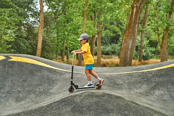 Boy riding scooter on a pumptrack at the park