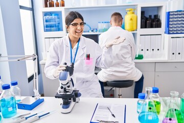 Young woman working at scientist laboratory celebrating achievement with happy smile and winner expression with raised hand