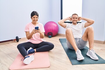 Man and woman couple smiling confident training abs exercise using smartphone at sport center