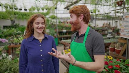 A male florist speaking with female customer inside Flower Shop. Local Business concept of worker wearing green apron assisting client