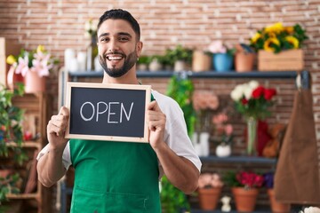 Hispanic young man working at florist holding open sign smiling and laughing hard out loud because funny crazy joke.