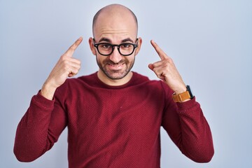 Naklejka premium Young bald man with beard standing over white background wearing glasses smiling pointing to head with both hands finger, great idea or thought, good memory