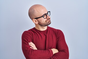 Young bald man with beard standing over white background wearing glasses looking to the side with...